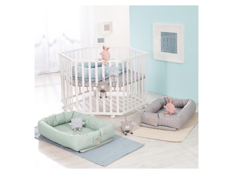 Lit bébé hexagonal blanc avec matelas bleu, deux nids bébé avec peluches et tapis.