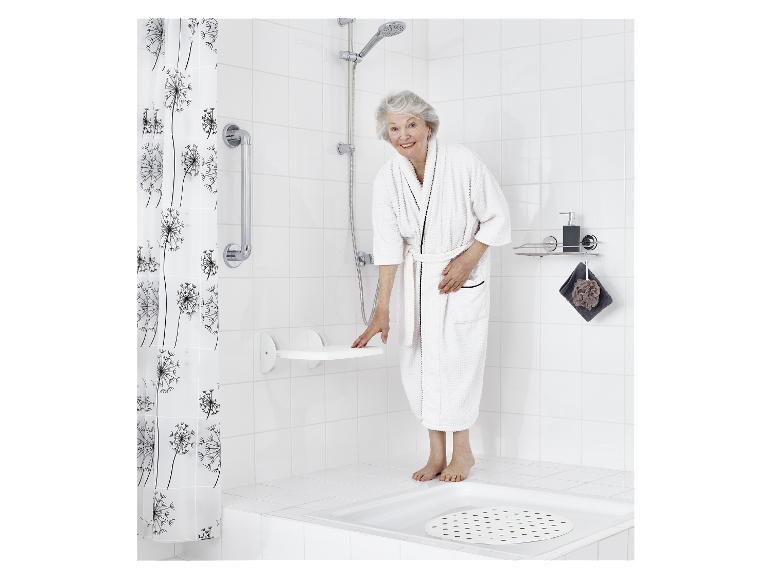 Une femme âgée en peignoir utilise un tabouret de douche pliable dans une salle de bain moderne.
