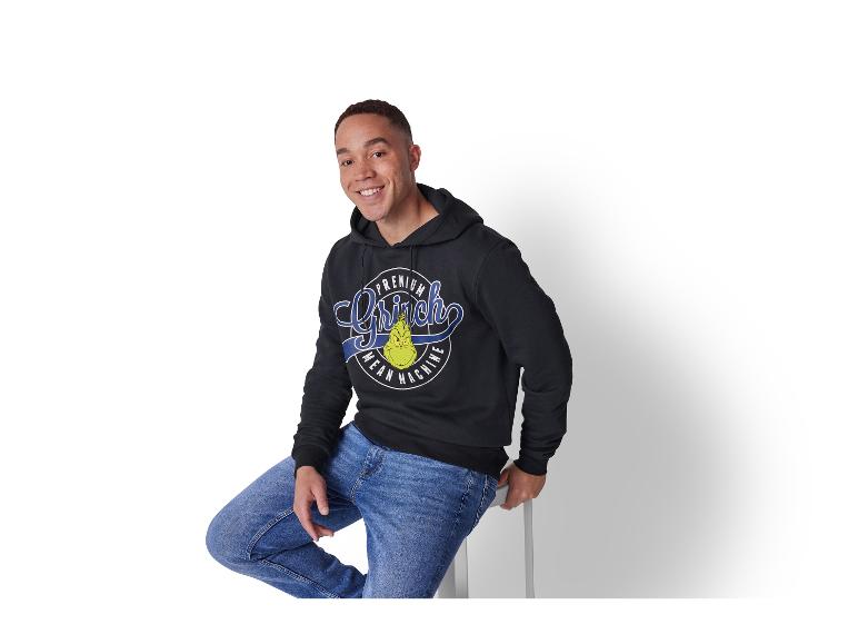 Homme souriant portant un sweat à capuche noir Grinch et un jean bleu.
