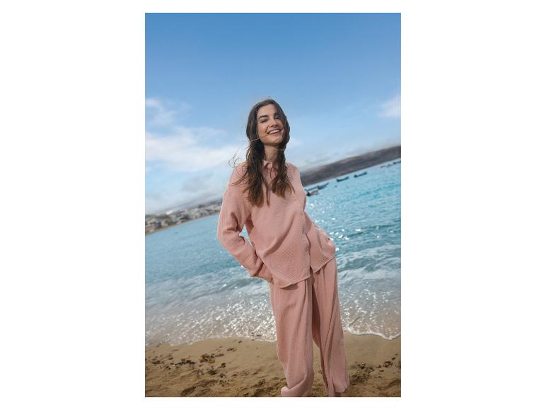 Femme souriante en ensemble rose sur la plage avec la mer en arrière-plan.