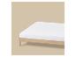 Drap-housse blanc sur un cadre de lit en bois clair.