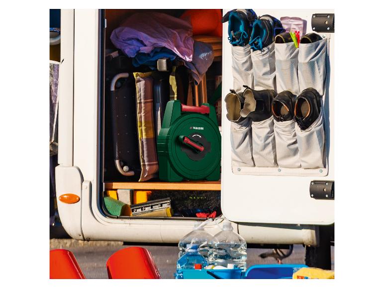 Rangement de camping-car ouvert avec un enrouleur de tuyau vert, des chaussures dans un organisateur suspendu et des produits de nettoyage.