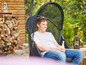 Un homme se détend dans un fauteuil suspendu avec une boisson dans le jardin.