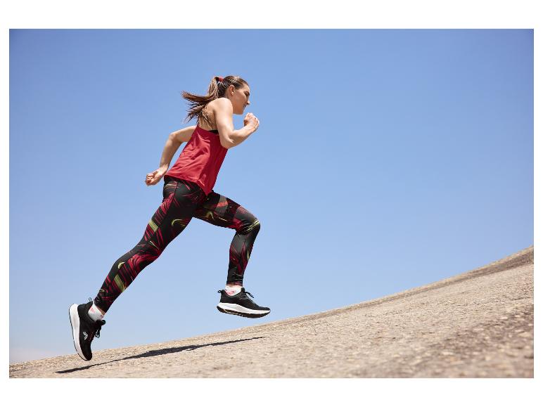 Femme courant en débardeur rouge et leggings à motifs sur fond de ciel bleu.