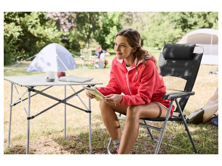 Femme assise sur une chaise de camping pliable, lisant une carte près d'une table de camping.
