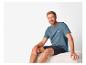 Homme souriant en t-shirt bleu imprimé et short bleu foncé.