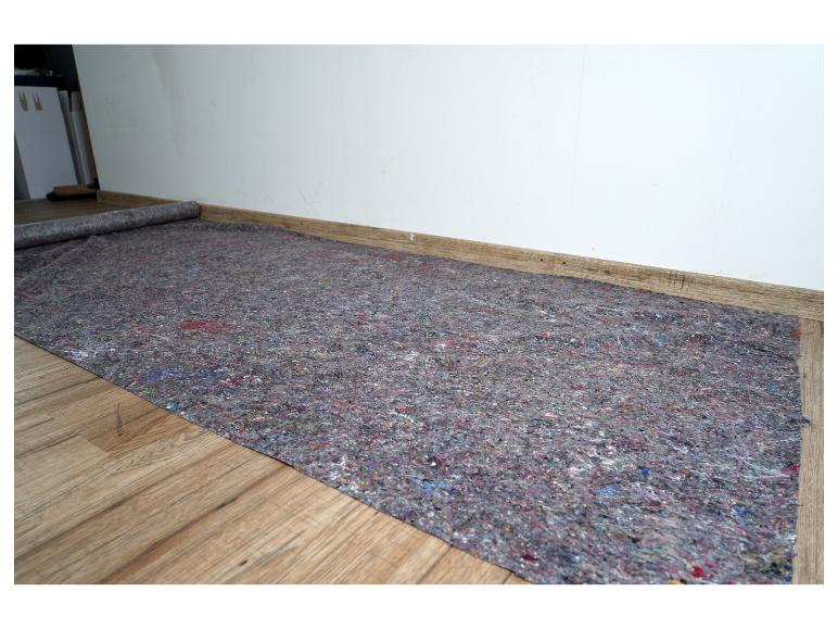 Feutre de protection étalé sur un parquet en bois à côté d'un mur blanc.