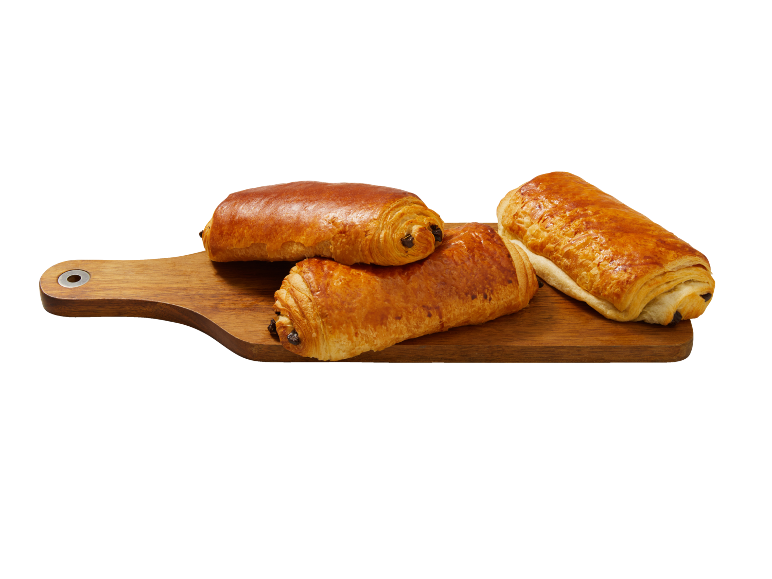 Trois pains au chocolat dorés sur une planche à découper en bois.