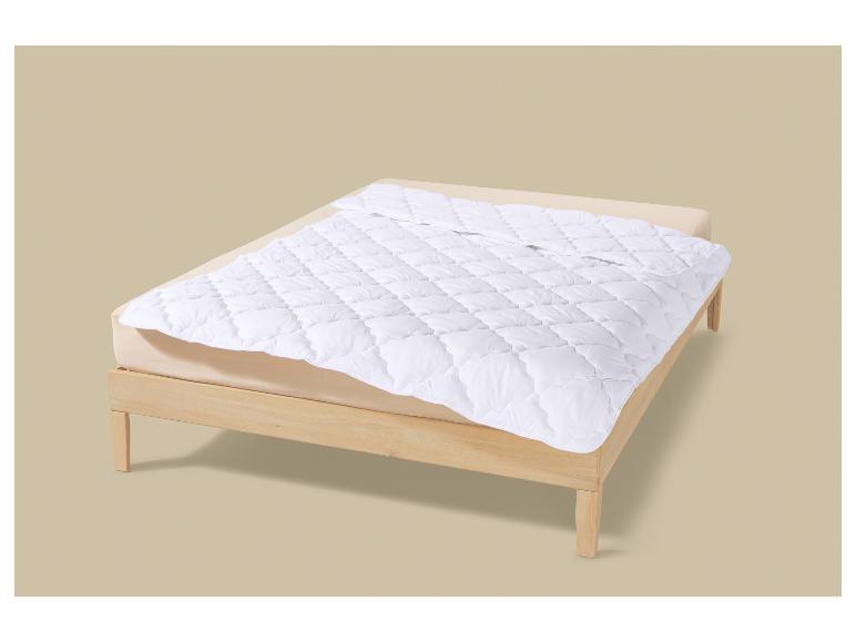 Un protège-matelas matelassé blanc sur un lit à cadre en bois.