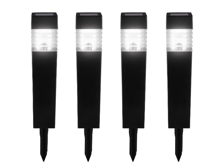 Quatre lampes solaires de jardin noires avec lumière blanche et piquets de terre.