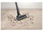 Aspirateur balai nettoyant un tapis, débris au sol.