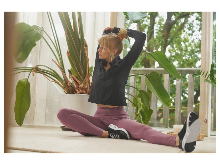 Femme en veste de sport noire et leggings violets s'étirant à l'intérieur.