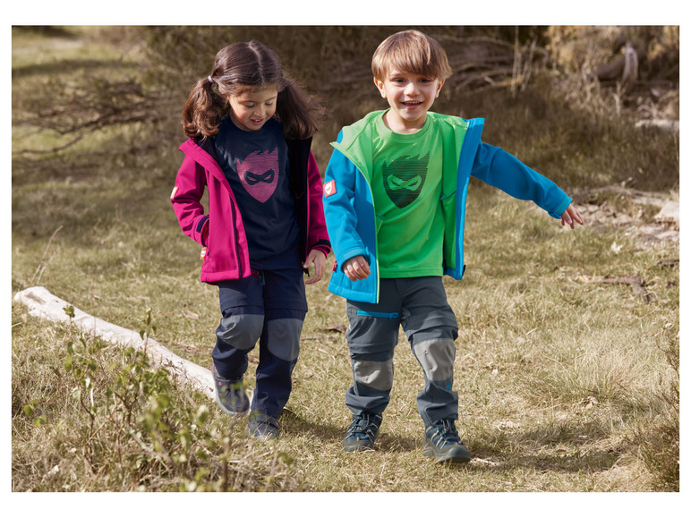 Deux enfants portent des vestes, des t-shirts et des pantalons à l'extérieur dans la nature.