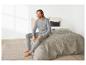 Un homme en pyjama gris assis sur un lit.