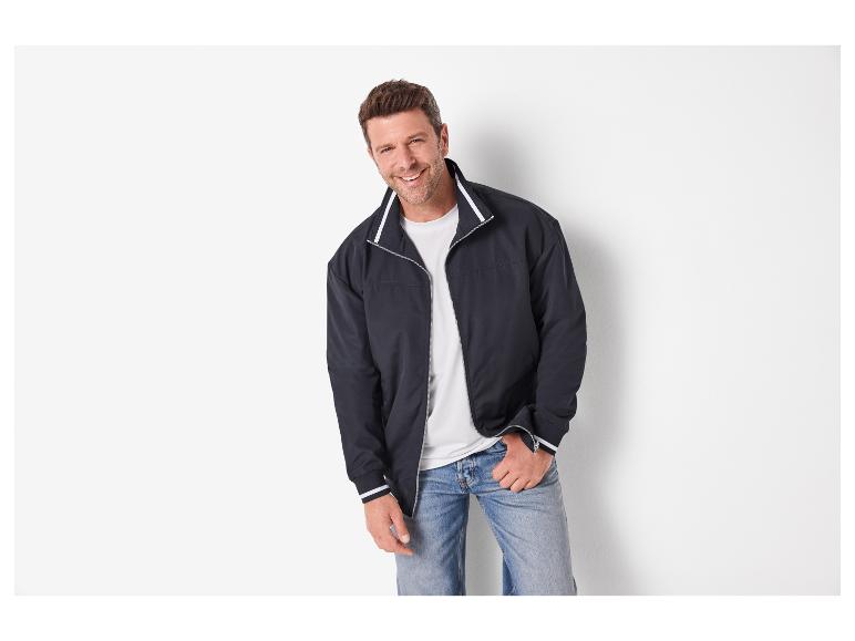 Homme souriant portant une veste bleu marine, un t-shirt blanc et un jean.