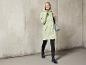 Une femme porte un imperméable vert et des bottes de pluie bleues.