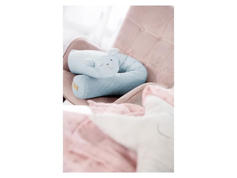 Oreiller bleu matelassé en forme de lapin sur un fauteuil rose, avec une couverture rose et un oreiller blanc au premier plan.