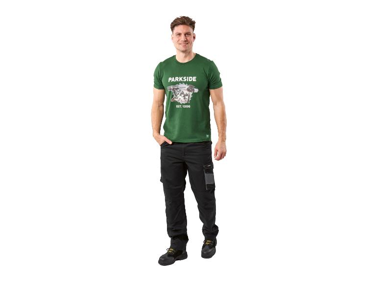 Homme en T-shirt vert avec imprimé d'outils et pantalon de travail noir.