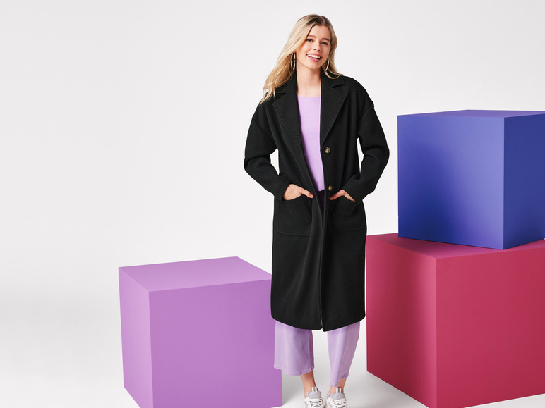 Une femme pose avec un manteau noir, un pantalon violet et des baskets blanches.