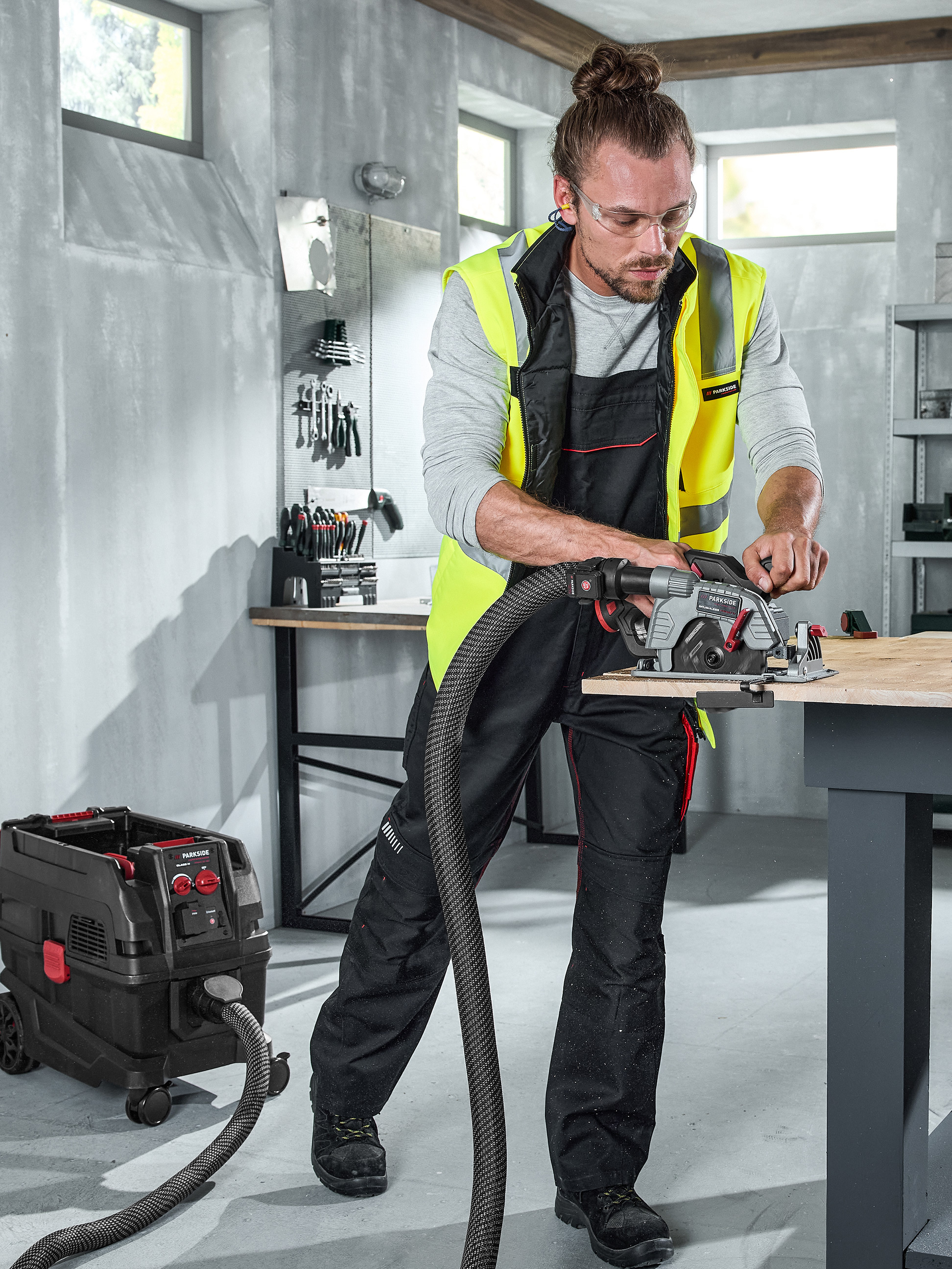 Homme coupant du bois avec une scie connectée à un aspirateur dans un atelier.