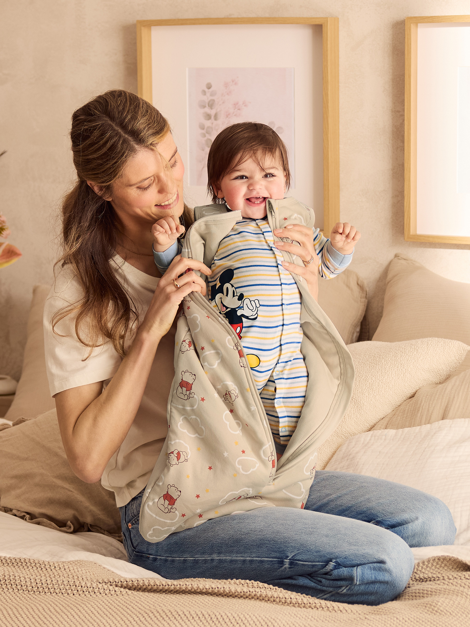 Mère souriante tenant un bébé rieur dans une gigoteuse à motifs de Winnie l'Ourson.