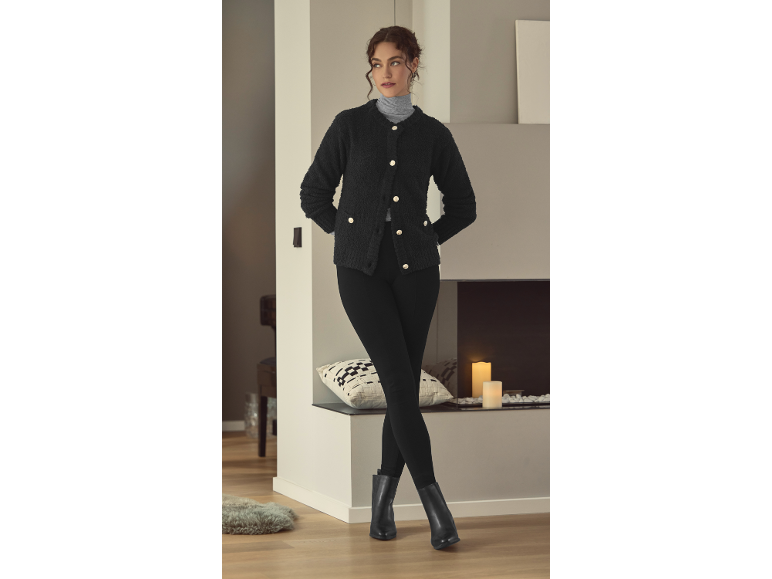 Femme en cardigan noir, col roulé et leggings, posant dans une pièce confortable.