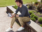 Un homme vêtu d'un t-shirt gris et d'un pantalon beige lit un journal.