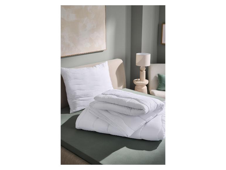 Oreiller matelassé blanc et couette pliée sur un lit avec un drap vert