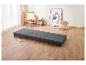 Matelas pliant gris sur un parquet clair dans une pièce avec une chaise et une œuvre d'art.