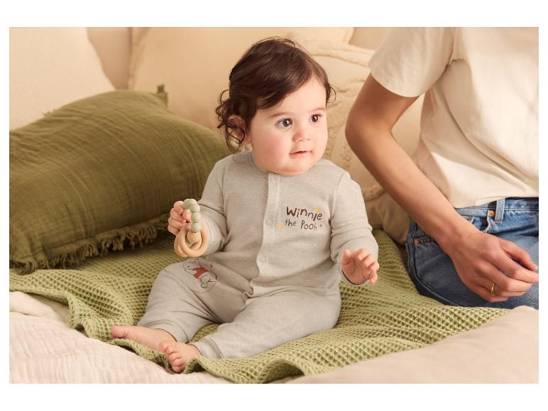 Bébé en grenouillère grise avec texte 'Winnie l'Ourson' et anneau de dentition, assis sur une couverture verte.
