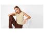 Femme en top beige brodé et pantalon marron, assise sur une chaise blanche.