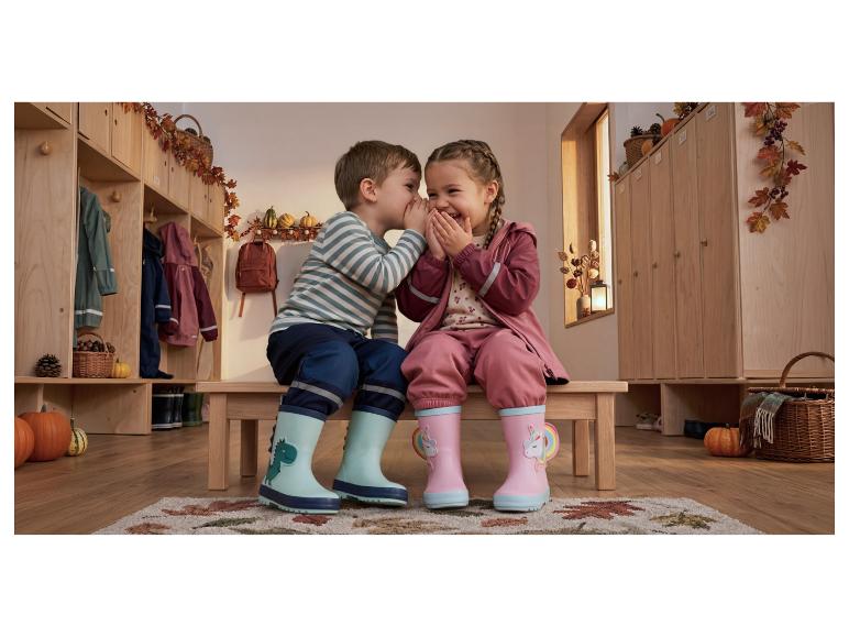 Deux enfants en cirés et bottes de pluie colorés chuchotent dans un vestiaire décoré d'automne.