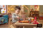 Petit garçon coupant une pizza jouet avec des couverts jouets à une table en bois dans une chambre d'enfant.