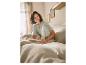 Femme souriante en pyjama vert clair lisant un livre au lit.
