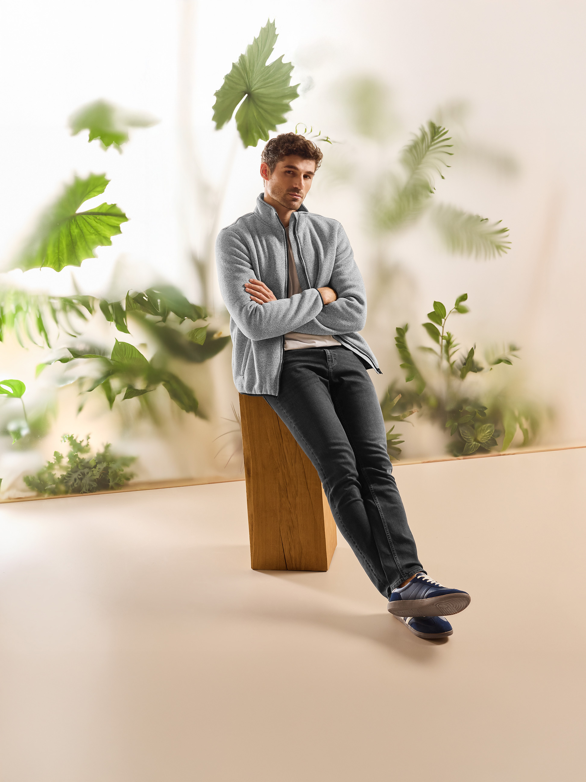 Homme en veste polaire grise et jean foncé, assis dans un cadre naturel.