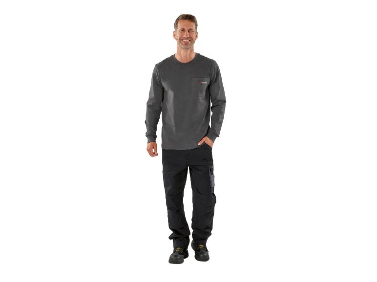 Homme souriant en t-shirt gris à manches longues et pantalon de travail noir