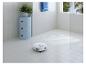 Robot aspirateur nettoyant une salle de bain carrelée avec un meuble bleu et une plante.
