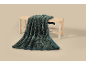 Couverture texturée vert foncé drapée sur un banc en bois avec assise tressée.