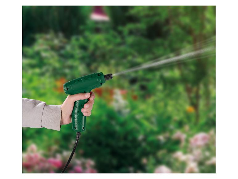 Pistolet pulvérisateur vert tenu à la main, projetant de l'eau dans un jardin verdoyant.