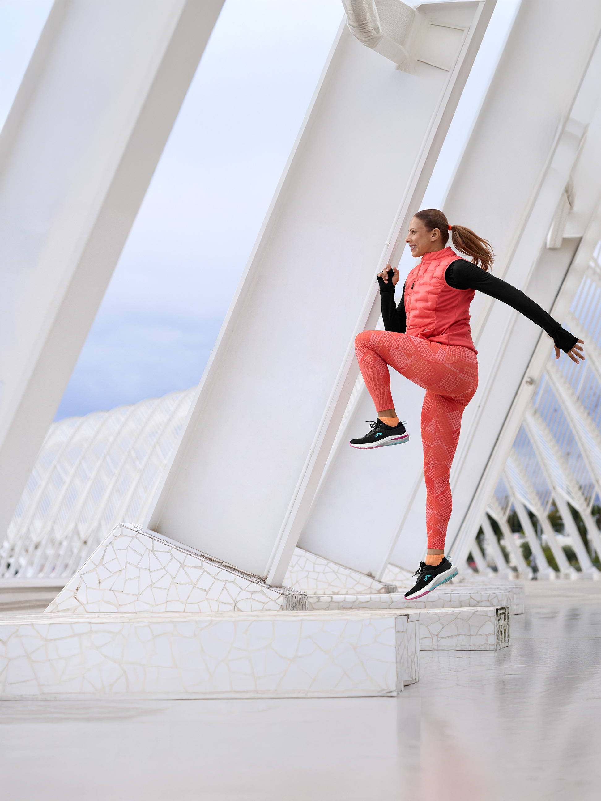 Femme en tenue de sport corail et noire, faisant de l'exercice sur une structure blanche moderne.