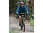 Un homme sur un VTT, avec une veste bleue, traverse une forêt.