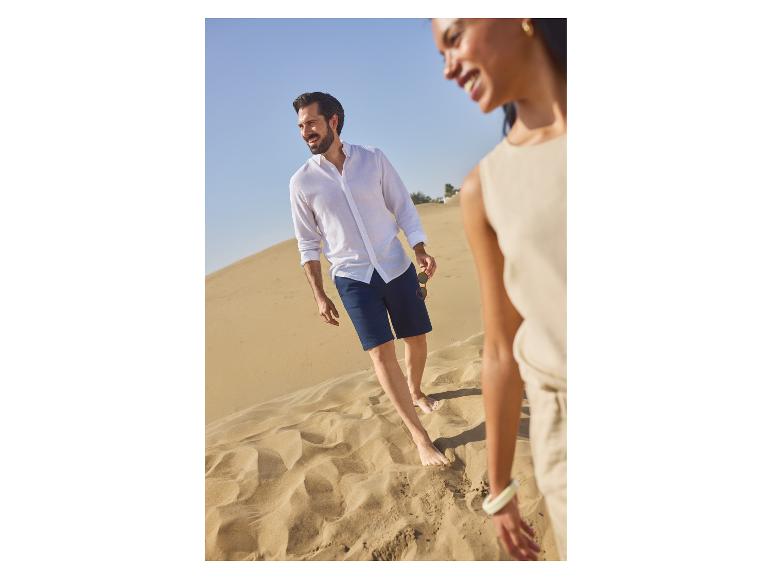 Homme en chemise de lin blanche et short bleu marine marchant pieds nus sur les dunes avec une femme.