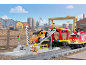 Train jouet avec wagon de transport de voitures et figurines dans un décor industriel.