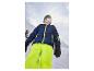 Garçon heureux en veste et pantalon de ski bleus et vert fluo sur une colline enneigée.