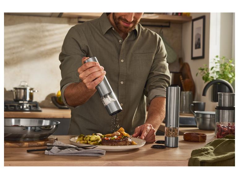 Un homme assaisonne un steak avec un moulin à sel et à poivre électrique.