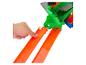 Main appuyant sur une piste de jouet orange avec une structure de jouet verte et grise en arrière-plan.