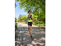 Femme courant dans un parc, vêtue d'un haut jaune fluo, d'un short noir et d'un gilet de course.
