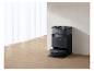 Robot aspirateur noir avec station de charge dans une pièce avec rideaux blancs et parquet.
