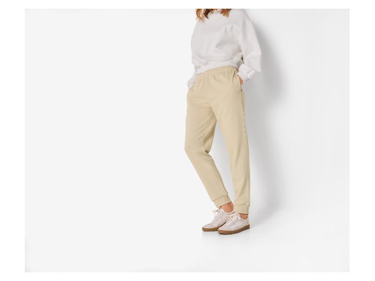 Femme portant un sweat-shirt beige et un pantalon de jogging beige sur fond blanc.