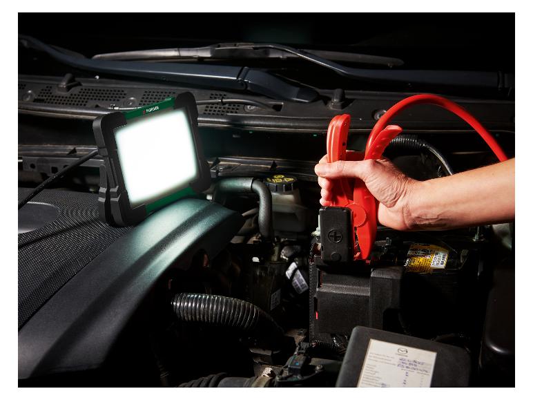 Lampe de travail LED et câbles de démarrage connectés à une batterie de voiture.